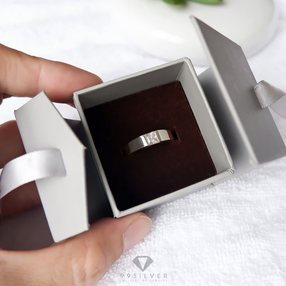กล่องใส่แหวนสีเทาสี่เหลี่ยม มีริบบิ้นผูกโบว์สำหรับยึดฝา ข้างในบุด้วยสปั้นช์นิ่มสีน้ำตาลเข้ม